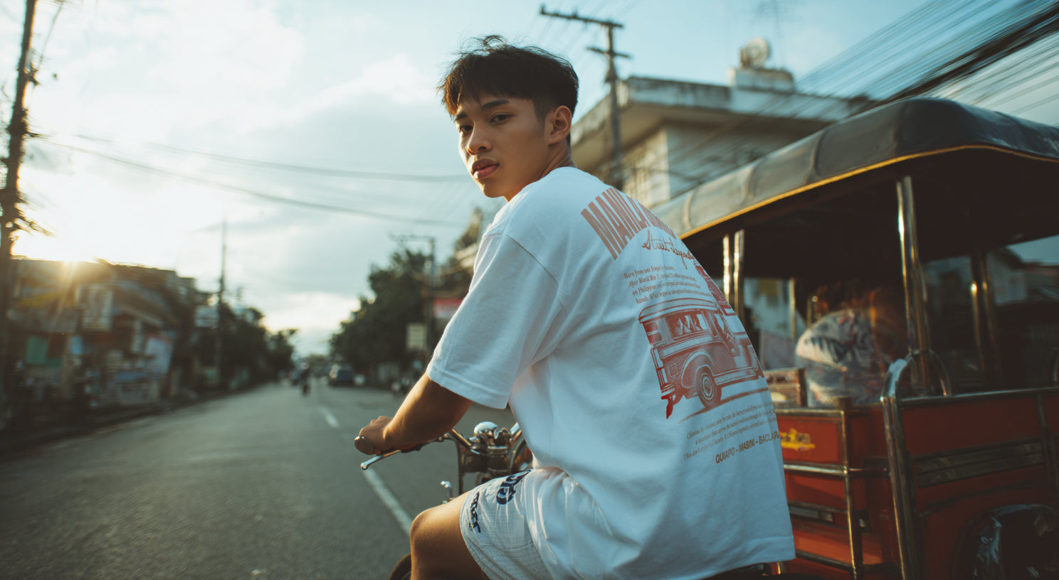 A filipino boy wearing a Manila Grand Prix  Shirt in white riding a bike in the streets of manila 